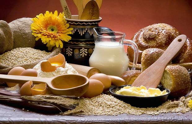 A jug of milk, eggs, a dish of butter and bread rolls on a kitchen table