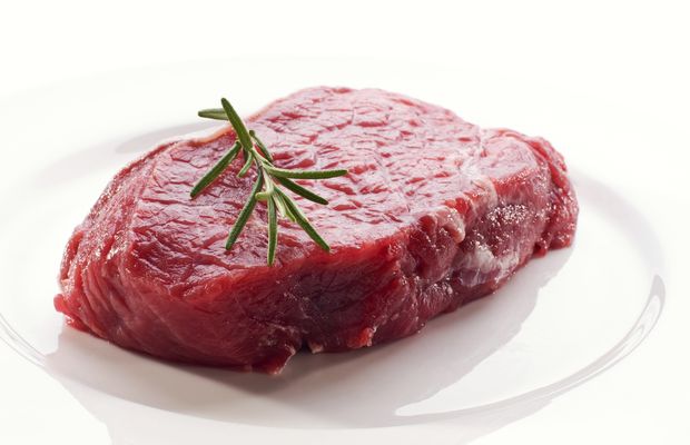 A raw beef steak with a sprig of rosemary on a white plate